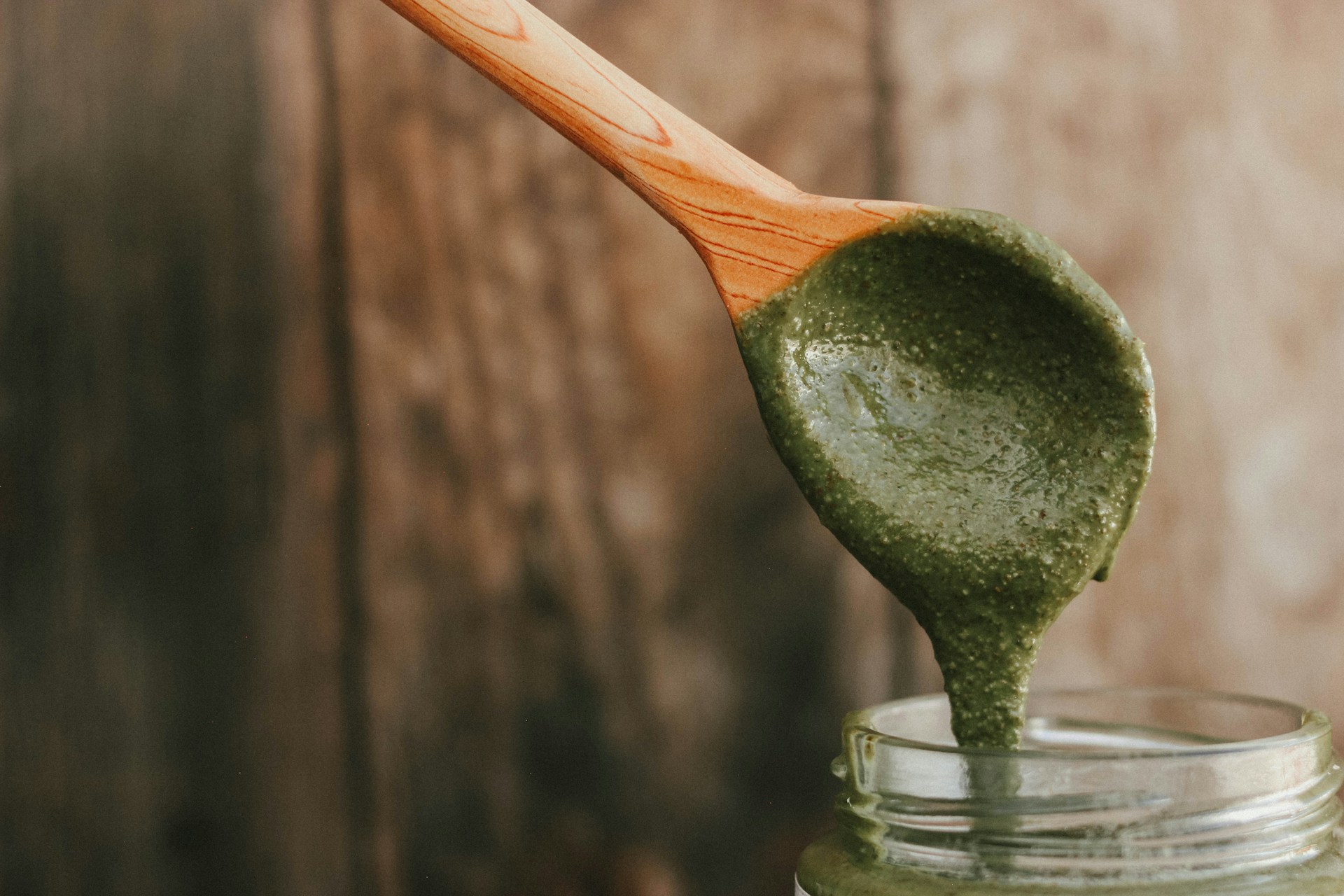 a wooden spoon full of green pest on top of a jar