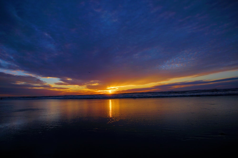 the sun is setting over the ocean on the beach