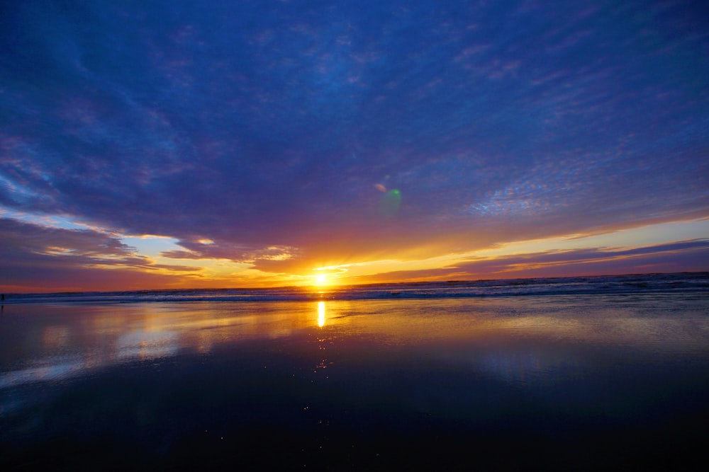 the sun is setting over the water at the beach