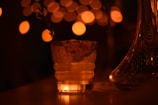 a glass of water on a table with lights in the background