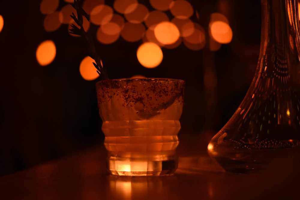 a glass of water on a table with lights in the background