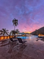 Spacious outdoor pool area surrounded by tropical plants at sunset