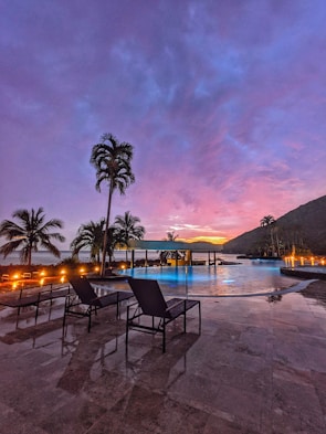 Spacious outdoor pool area surrounded by tropical plants at sunset
