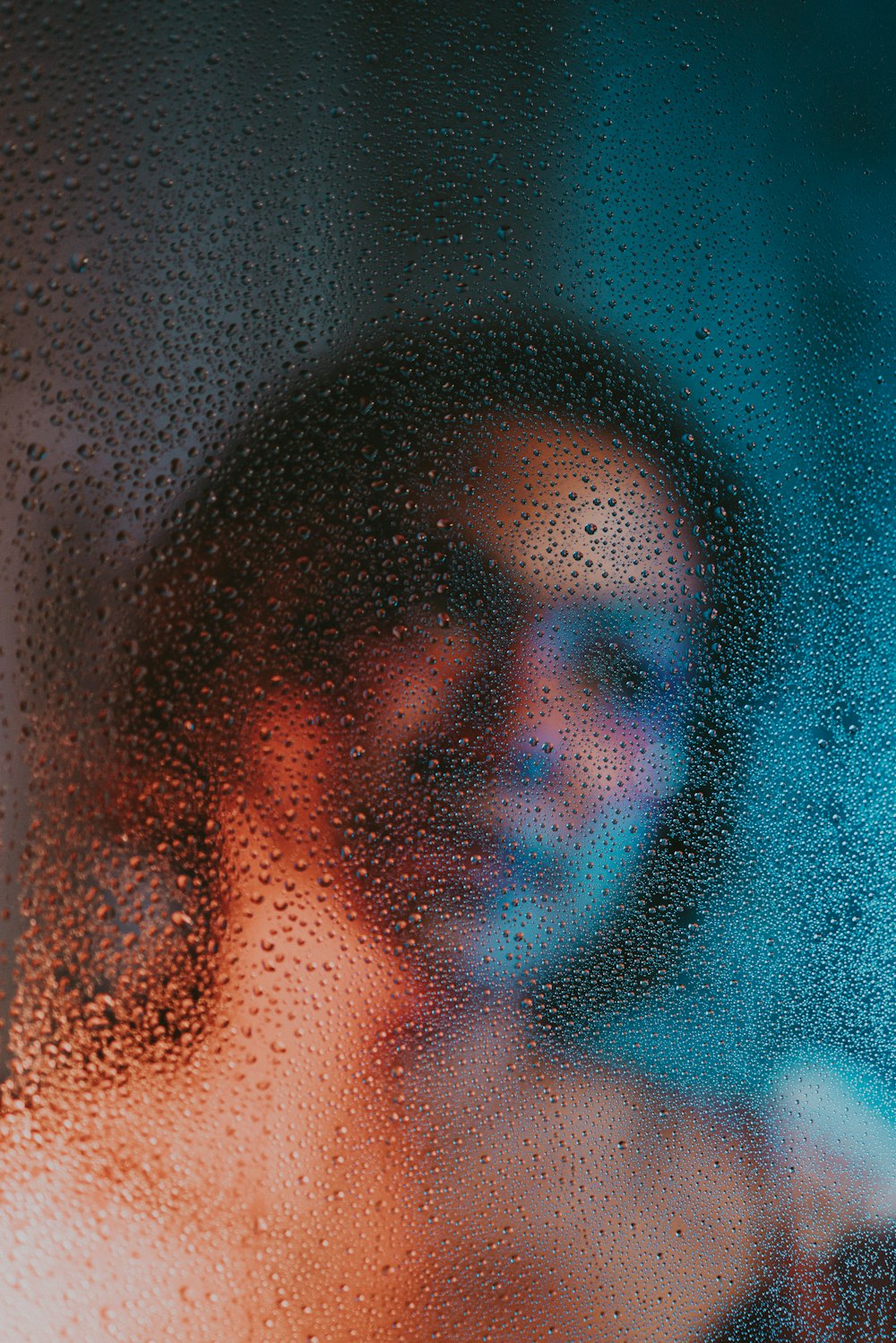 a woman standing behind a window covered in rain