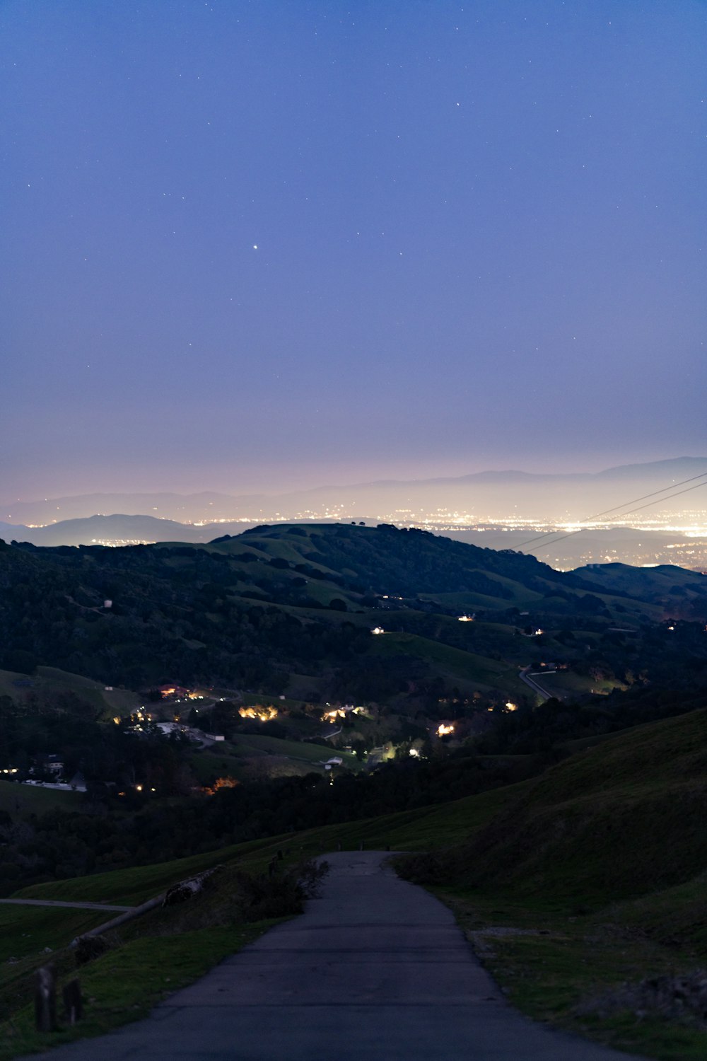 a view of the city lights from the top of a hill