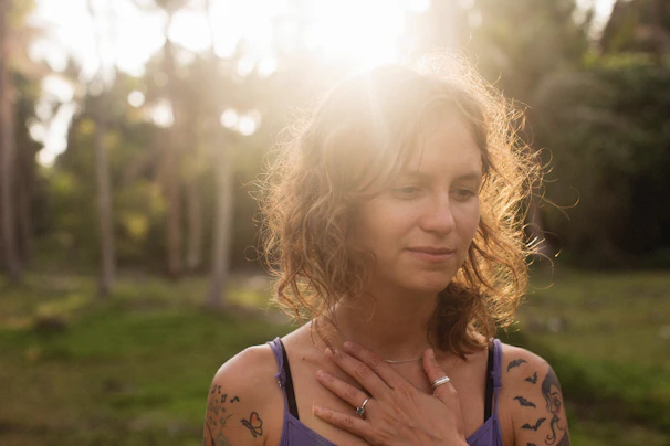 a woman with tattoos on her chest standing in a forest