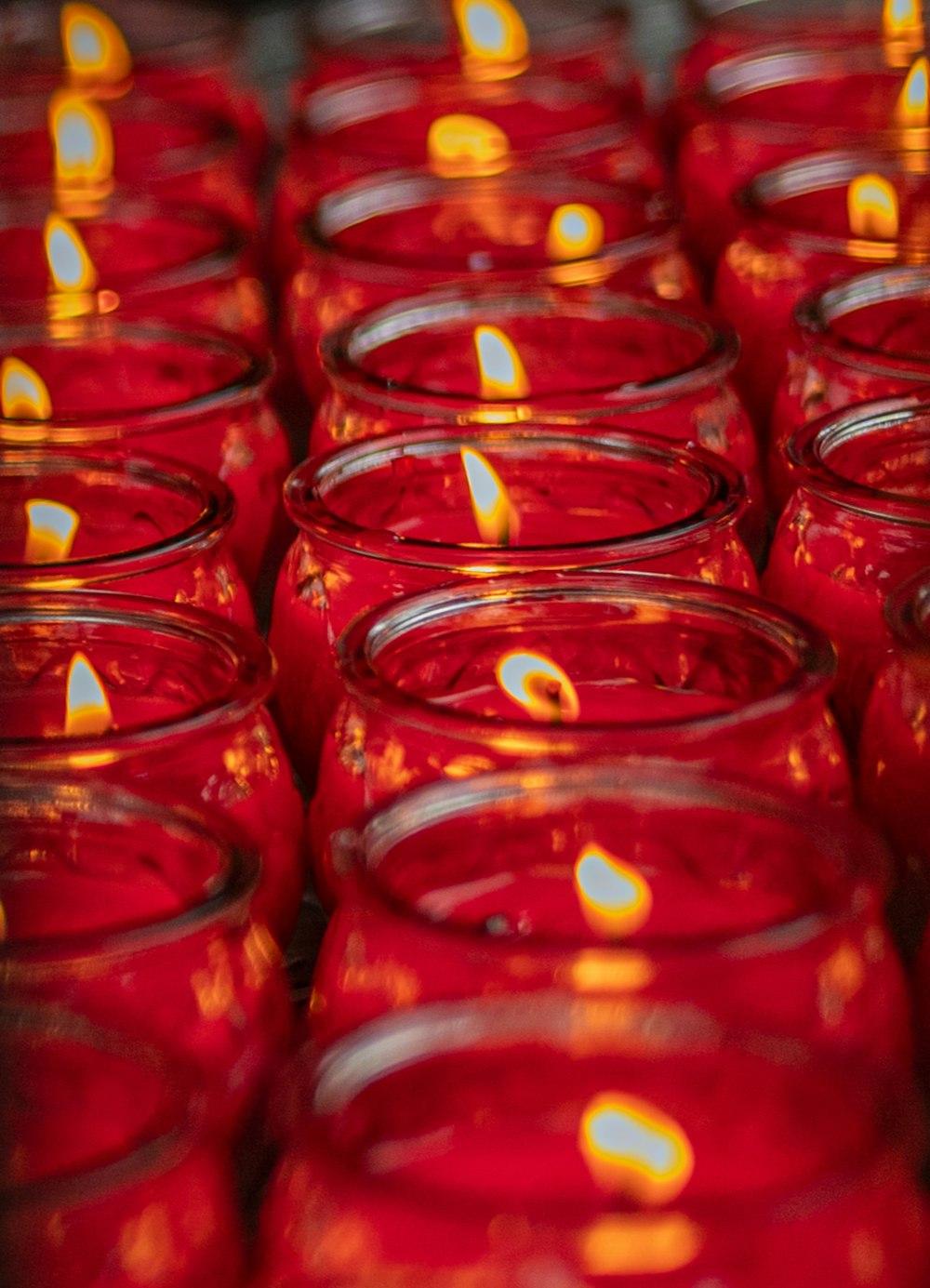 rows of red glass jars with lit candles in them