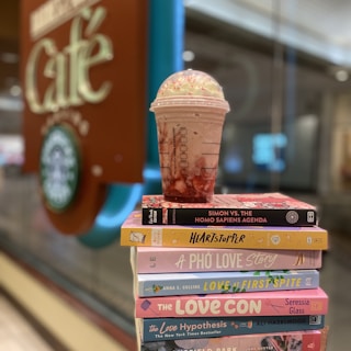 A stack of colorful books with a cup of coffee on a wooden table.