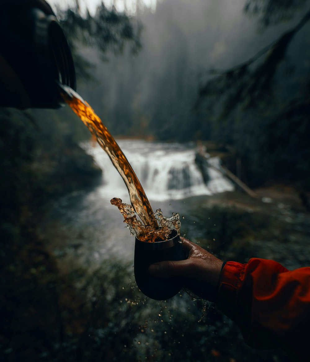 a person holding a glass with a liquid pouring out of it