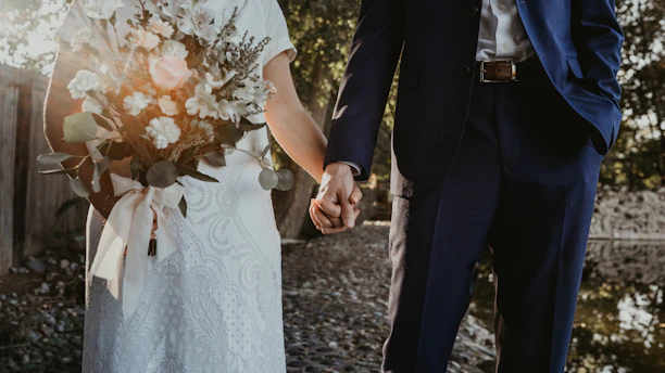 A couple holding hands with a musician playing guitar softly in the background during a wedding ceremony.