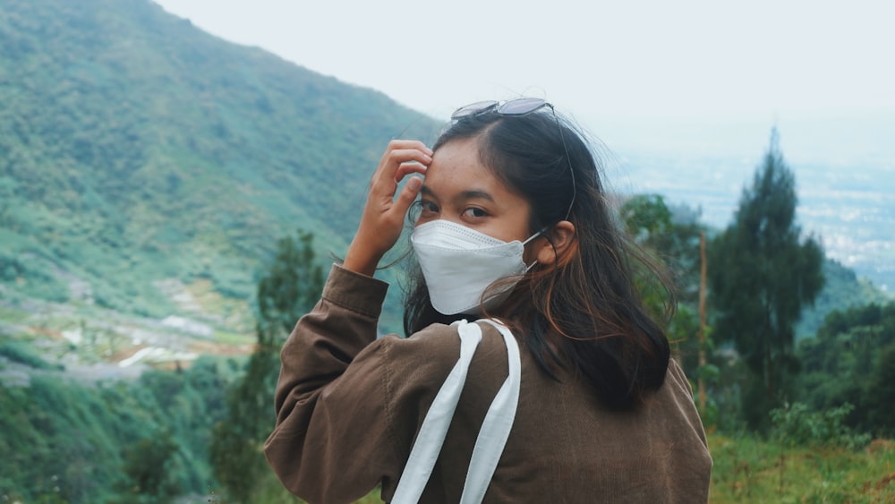 a woman wearing a face mask while standing on top of a hill