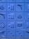 A series of blue blocks featuring various geometric shapes and patterns are displayed. The shapes include triangles, circles, arches, and lines carved into the blocks. The blocks are arranged in a grid pattern, creating a visually pleasing design with textured surfaces.