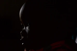 An artistic photo of a person silhouetted against a dimly lit background, emphasizing shadows and contrast