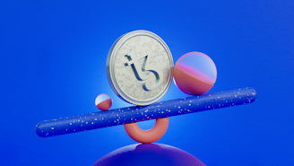 A Tezos cryptocurrency coin is balanced on a blue speckled cylinder. The setup includes a larger sphere with a pink and purple gradient and a smaller pink sphere. The background is vibrant blue.