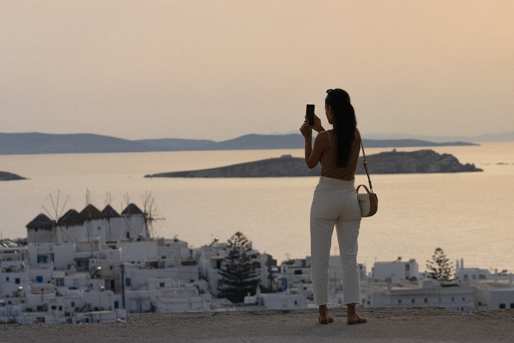 a woman taking a picture of the ocean with her cell phone