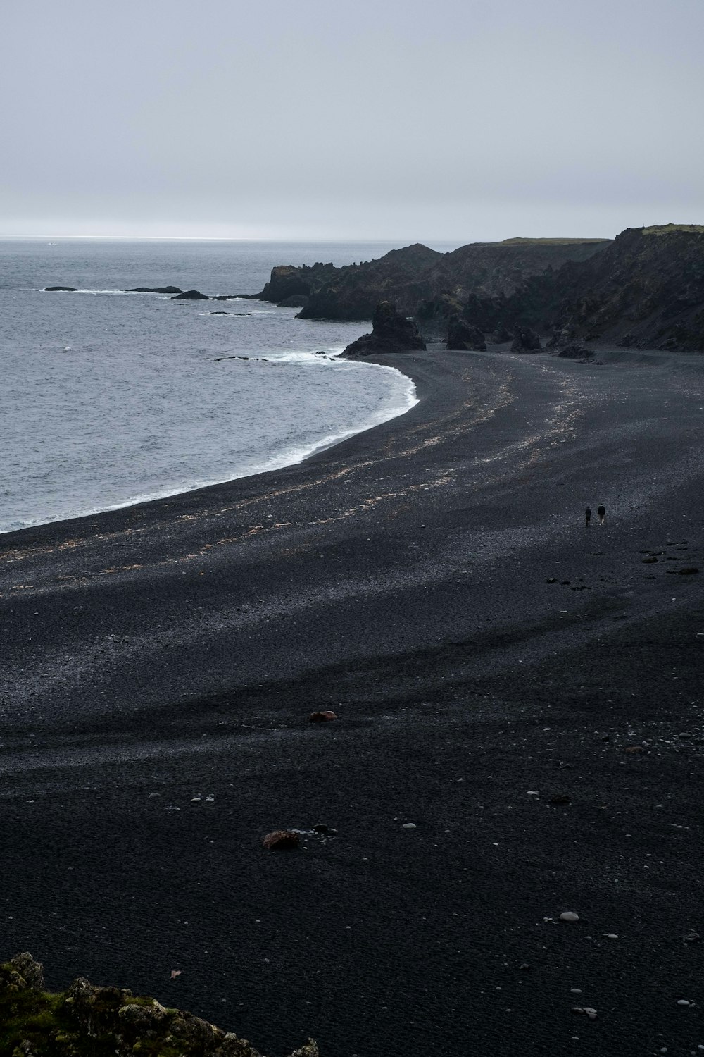 a couple of people walking along a beach next to the ocean