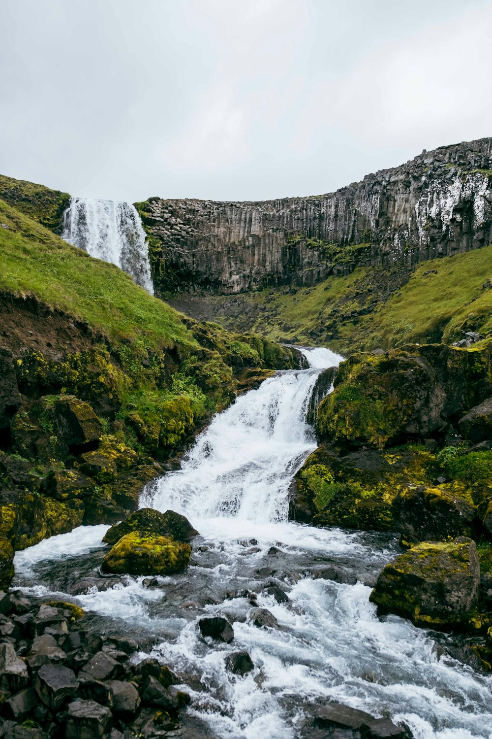 a small waterfall in the middle of a green valley