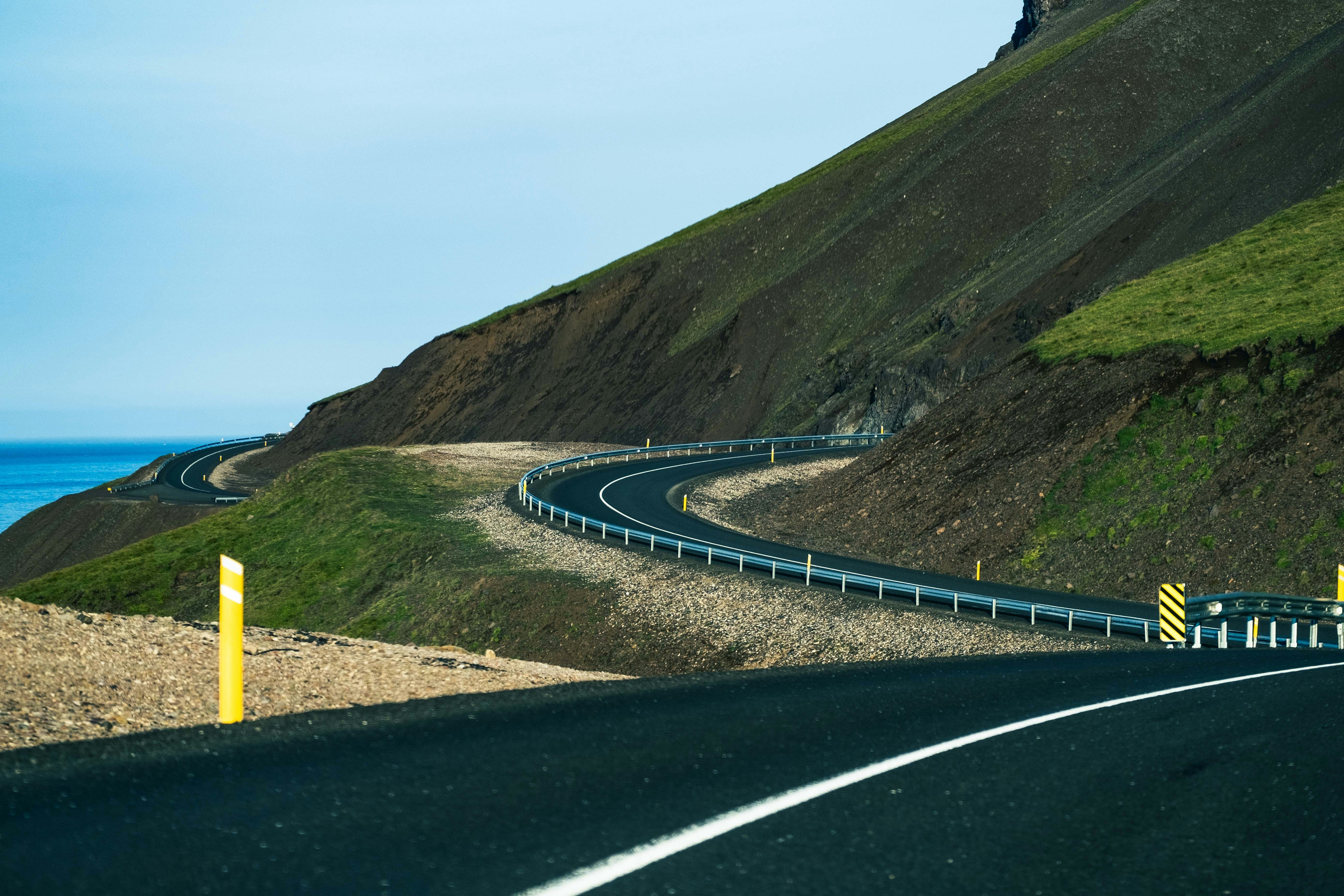 a curved road on the side of a hill next to the ocean