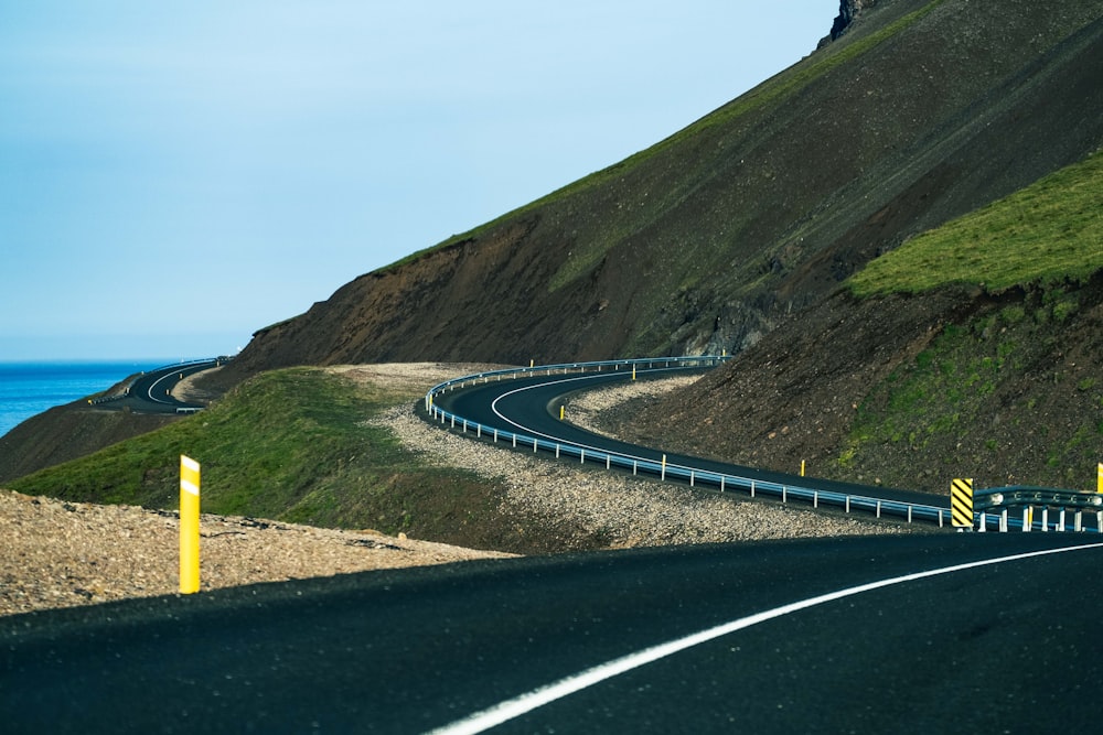 a curved road on the side of a hill next to the ocean