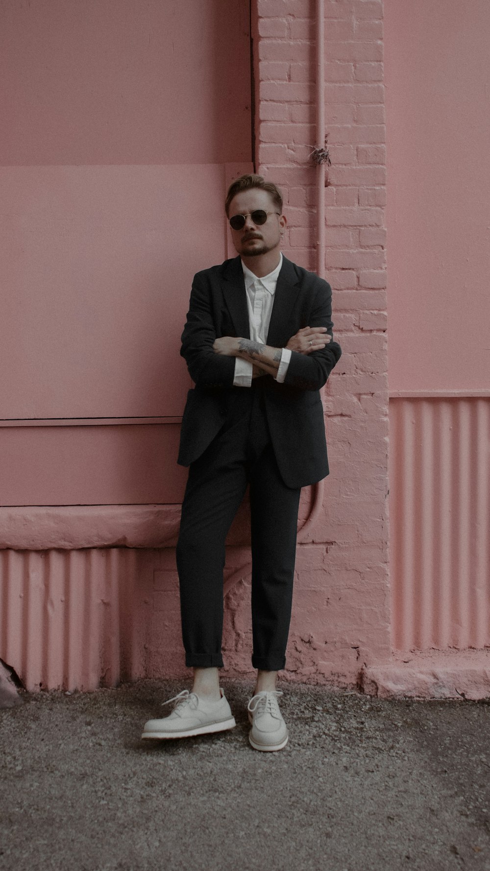 a man in a suit leaning against a pink wall