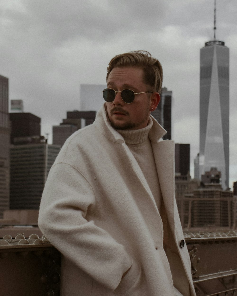 a man in a coat and sunglasses standing on a bridge