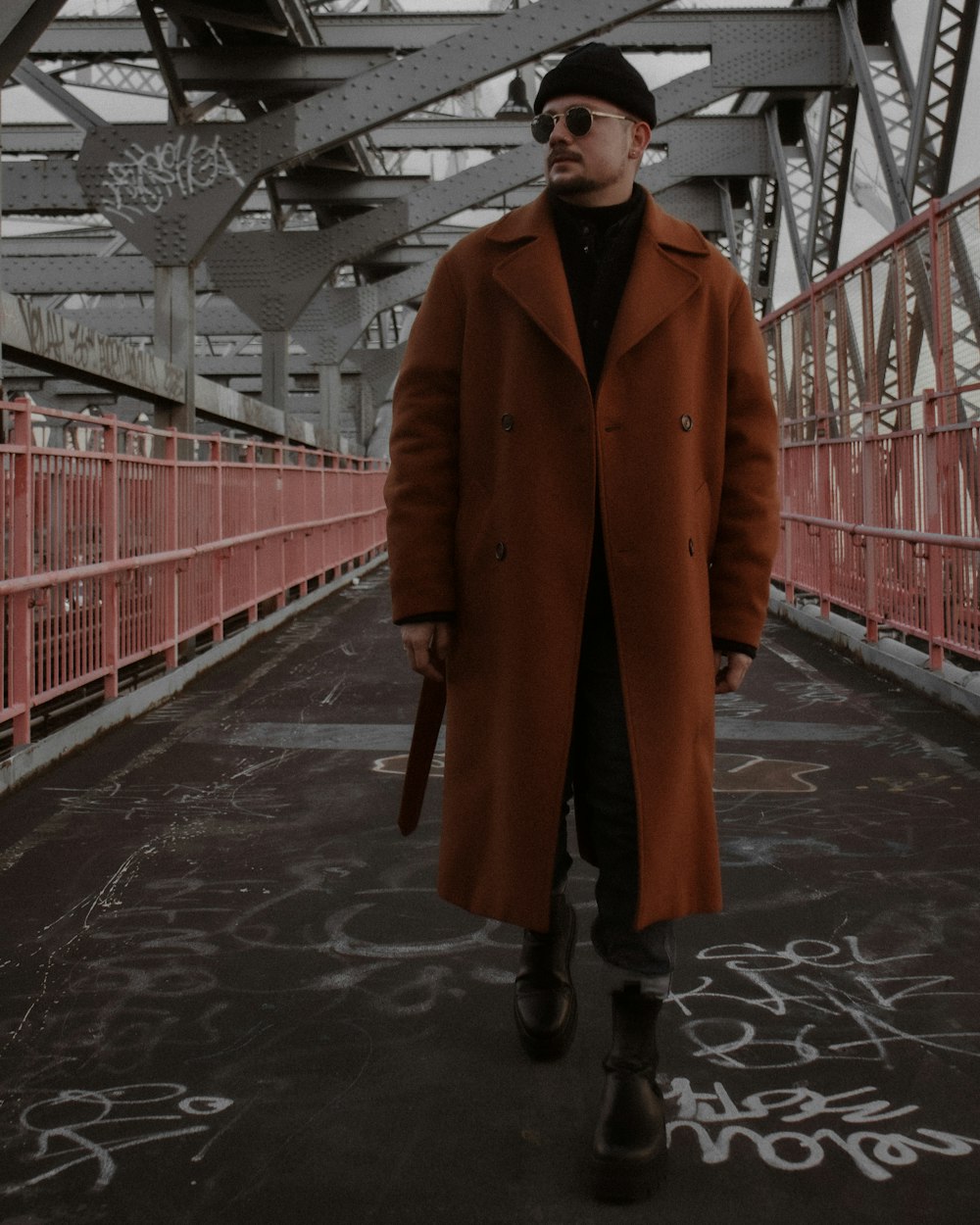 a man walking across a bridge wearing a brown coat