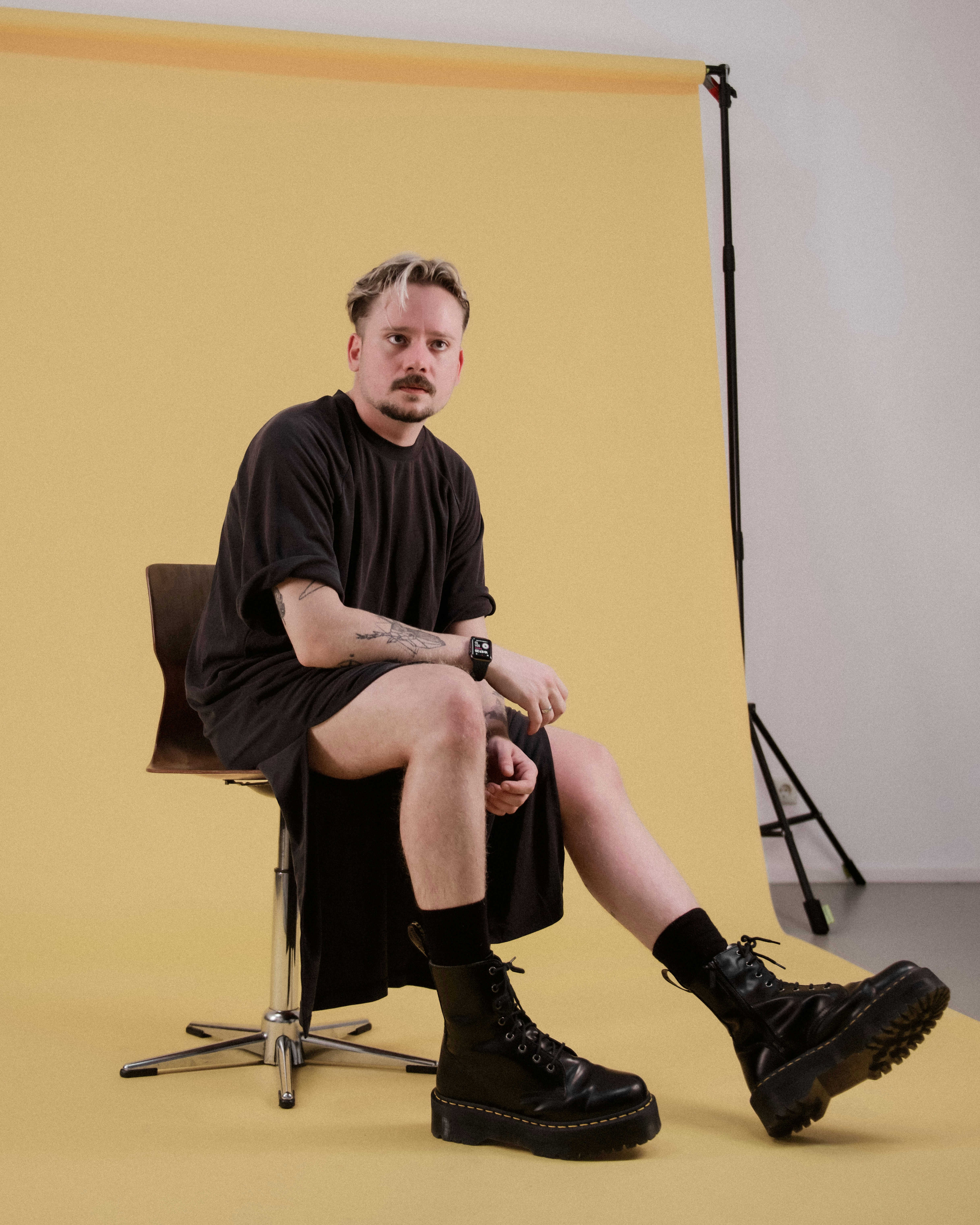 Minimalist siyah kıyafet ve platform botlarla oturan adam - cinsiyet akışkan stüdyo portresi