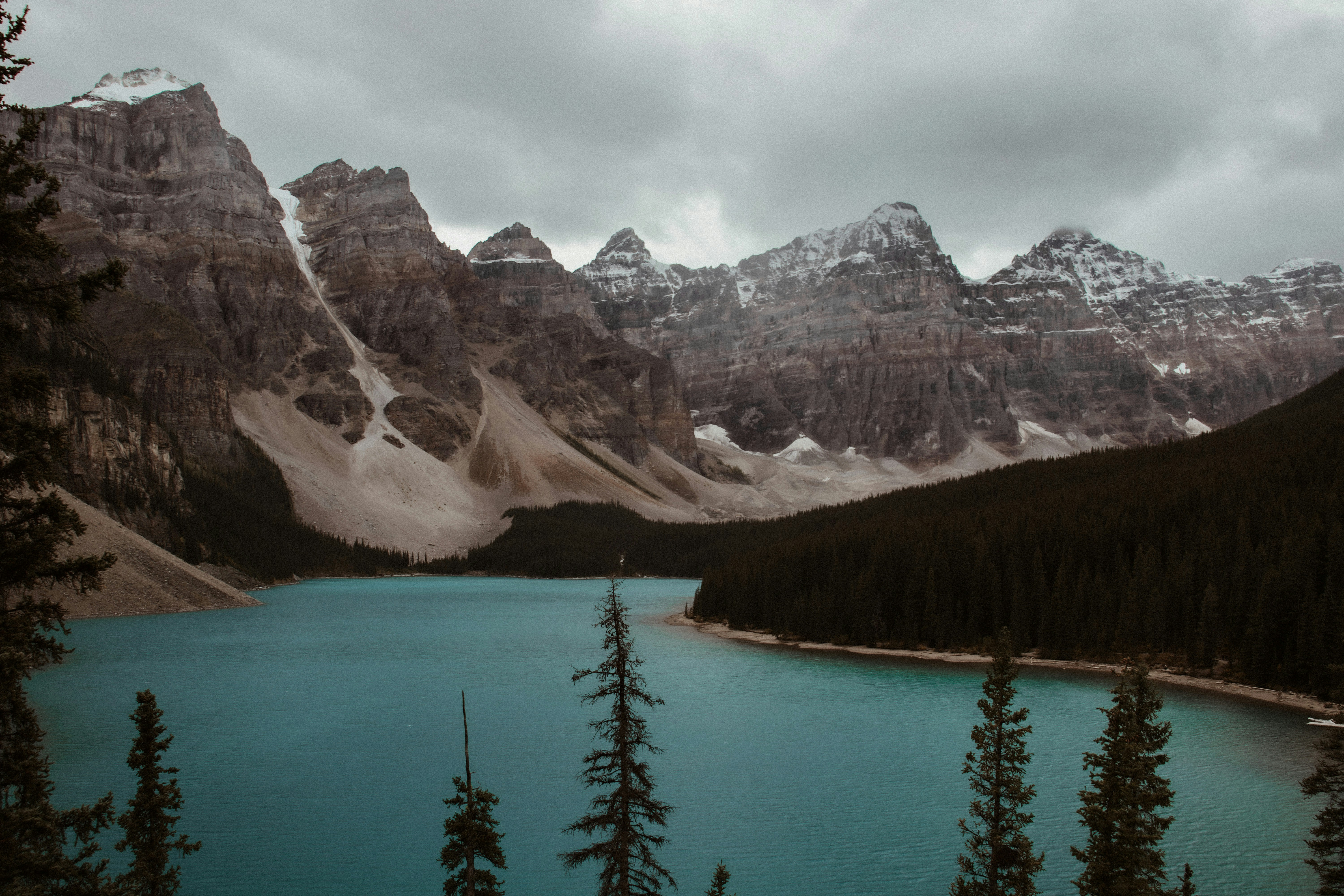 a lake surrounded by mountains and trees under a cloudy sky, 