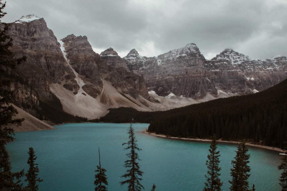 a lake surrounded by mountains and trees under a cloudy sky