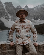 A rugged man wearing a heavy-duty jacket, standing confidently against a backdrop of mountains.