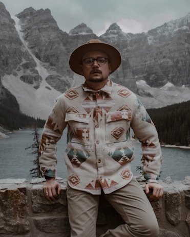 A rugged man wearing a heavy-duty jacket, standing confidently against a backdrop of mountains.
