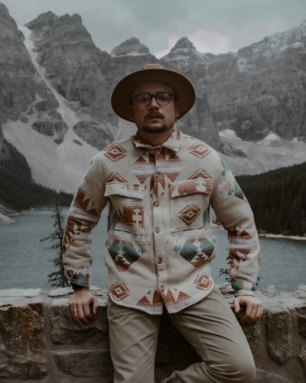 a man with a hat and glasses leaning on a wall