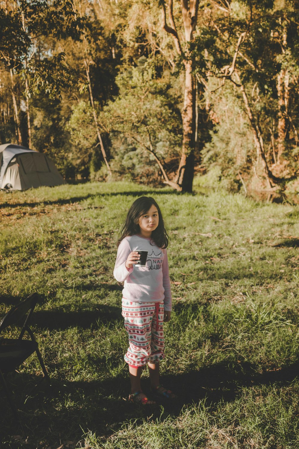 a little girl standing in the grass with a cell phone