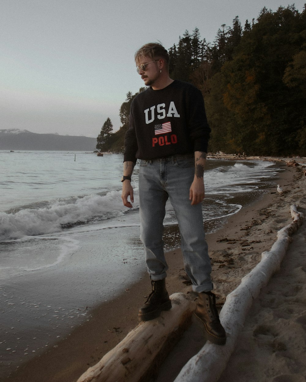 Ein Mann steht auf einem Baumstamm am Strand