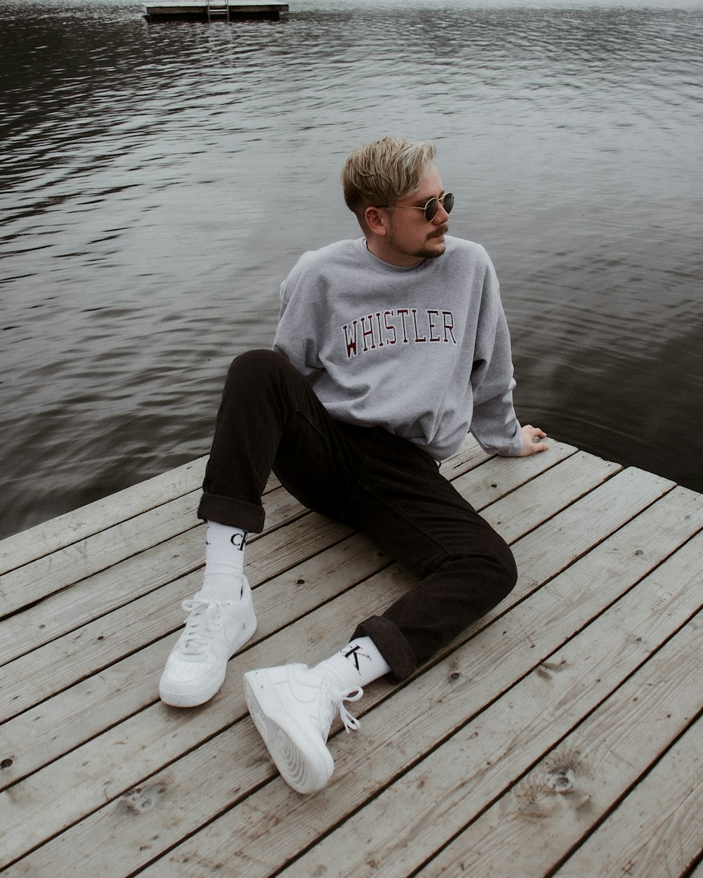 a man sitting on a dock next to a body of water