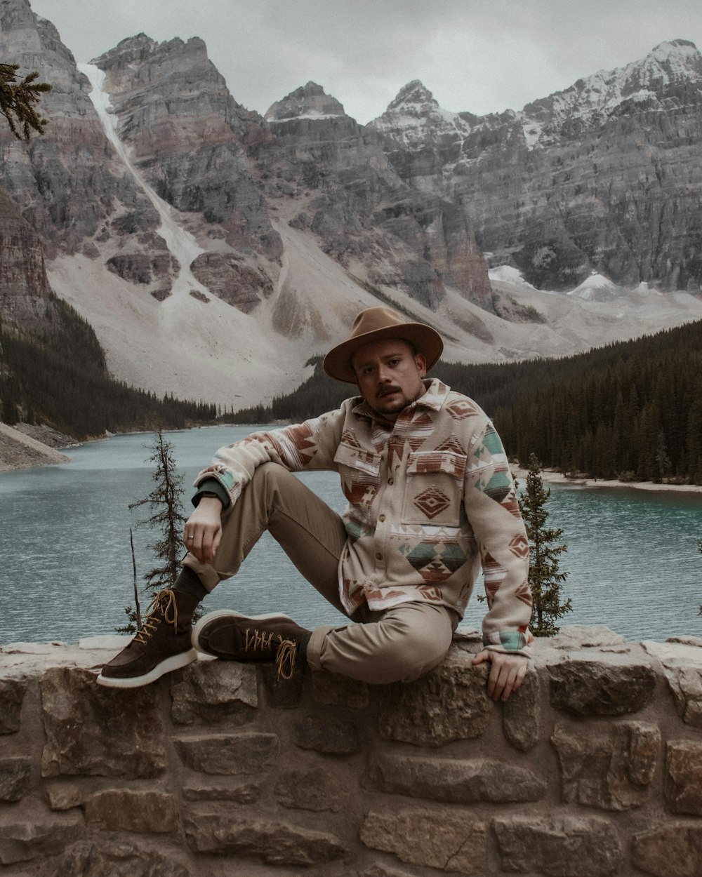 a man sitting on a stone wall next to a lake