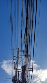 Numerous power lines crisscrossing the sky, connected to a utility pole with several transformers and insulators. The background features a clear blue sky with a few scattered clouds.