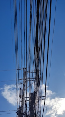 Numerous power lines crisscrossing the sky, connected to a utility pole with several transformers and insulators. The background features a clear blue sky with a few scattered clouds.