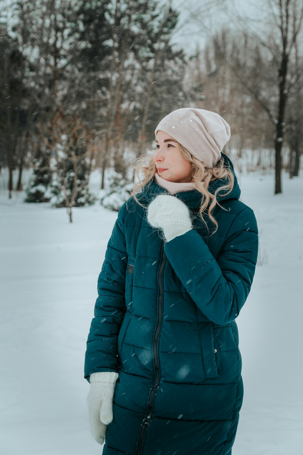 a woman standing in the snow wearing a green coat