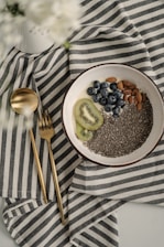 Close-up of fresh chia seeds spilling from a rustic wooden scoop onto a natural linen cloth.