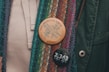 A close-up of two buttons pinned to a multicolored, textured fabric. The upper button is wooden with a design of a rose and the words 'TRY NONVIOLENCE' and 'REHUMANIZEINTL.ORG'. The lower button is black with '2,363 2363.ORG' in white text.