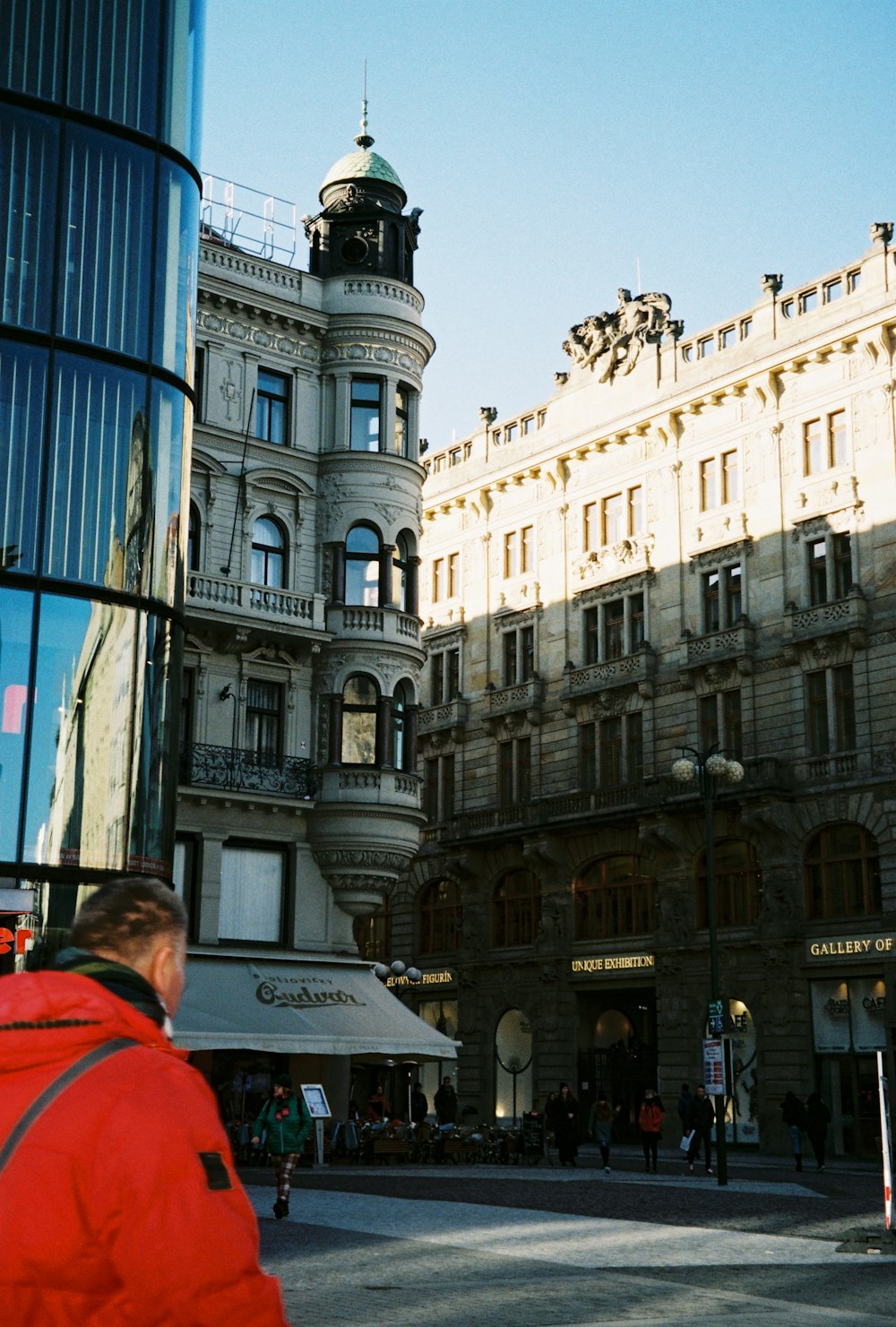 a man in a red jacket walking past a tall building