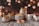 A collection of scented candle jars of various sizes and designs is arranged on a rustic wooden surface. The jars are labeled with the words 'Scented Candle Jar.' The background features a bokeh effect with warm, golden lights, creating a cozy atmosphere.