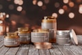 A collection of scented candle jars of various sizes and designs is arranged on a rustic wooden surface. The jars are labeled with the words 'Scented Candle Jar.' The background features a bokeh effect with warm, golden lights, creating a cozy atmosphere.