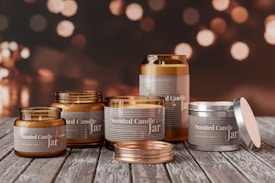 A collection of scented candle jars of various sizes and designs is arranged on a rustic wooden surface. The jars are labeled with the words 'Scented Candle Jar.' The background features a bokeh effect with warm, golden lights, creating a cozy atmosphere.