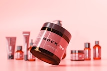 A collection of cosmetic containers arranged on a soft pink background with the largest container prominently in the foreground. The containers vary in size and shape, featuring a consistent color scheme with a focus on a mock-up design. The scene has a minimalist and modern aesthetic, highlighting the product design.