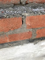 Close-up of weathered brick chimney needing repair, with cracked mortar and loose bricks.
