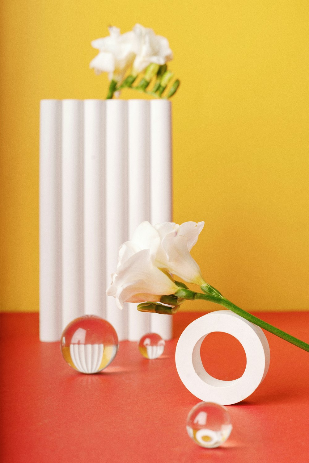 a white vase with a flower in it on a red table