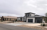 Modern suburban houses with clean lines and a minimalist design are visible. The first house has a multi-car garage and is painted in neutral colors with dark accents. The landscaping includes rocks and drought-resistant plants.