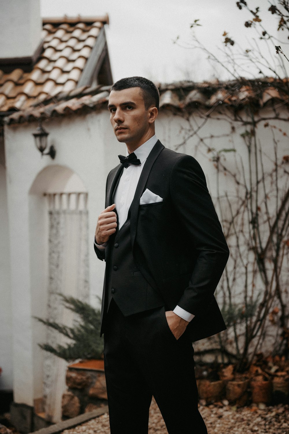 a man in a tuxedo standing in front of a house